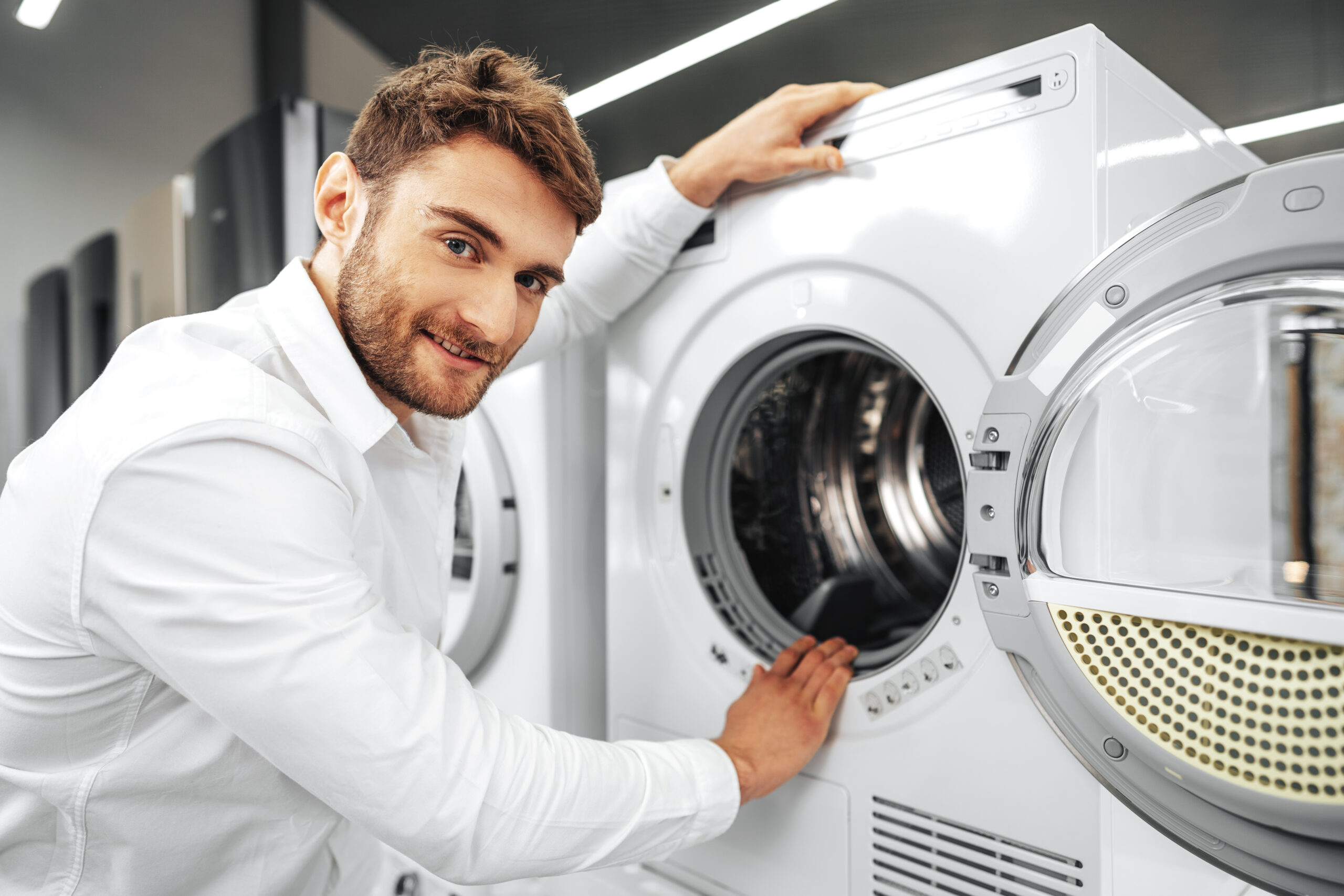 young man choosing new washing machine in household appliances store scaled